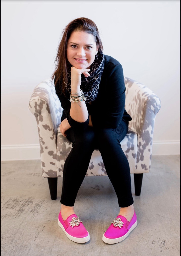 Smiling, beautiful brunette woman poses for a photo on a chair in her pink shoes.