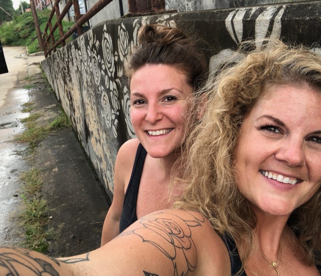 Two smiling women taking a selfie in front of a wall decorated with Clean Graffiti roses in Charlotte, NC.