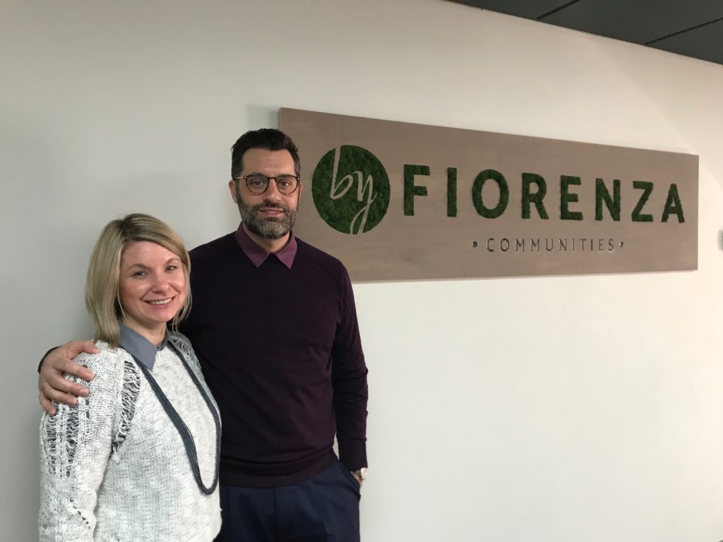a man and a woman standing shoulder to shoulder in front of the byFiorenza Moss Art sign.