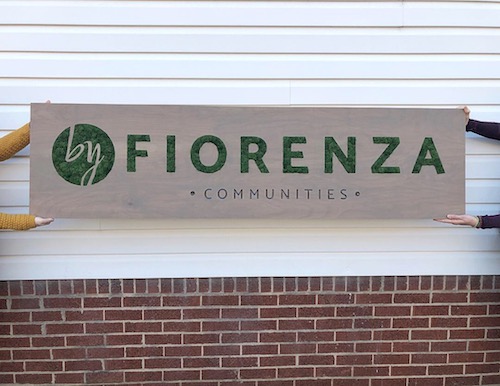 two people are holding up a Moss Art sign for byFiorenza Communities.