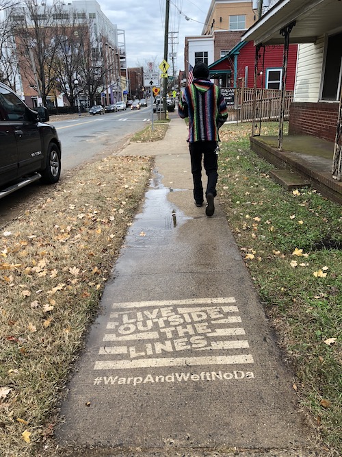 Guy walking in an artsy neighborhood over a sidewalk Clean Graffiti ad that says "Live Outside the Lines."