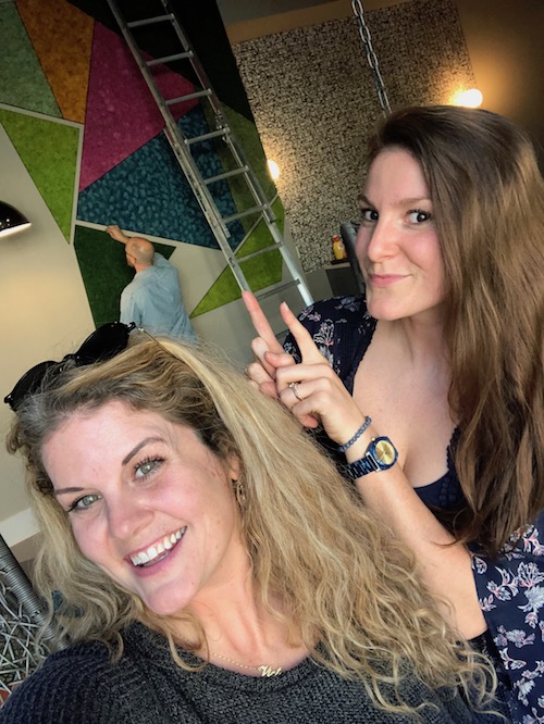 two smiling business owners point at their moss art labor of love going up in an apartment complex.