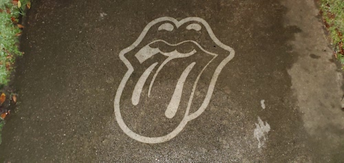 Image of the Rolling Stones famous mouth that is pressure washed into the dirty concrete of the sidewalk.
