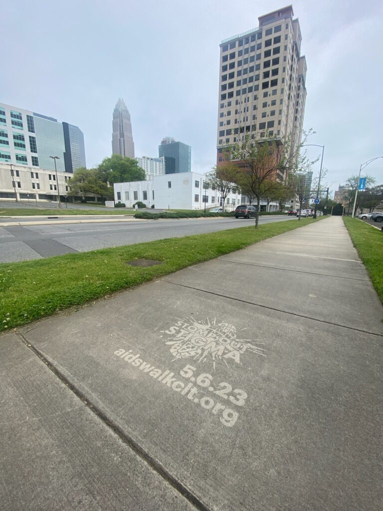 Clean Graffiti, aka pressure washed message of "Stomp Out Stigma. AIDS Walk Charlotte" on Charlotte, NC city sidewalk by The Savage Way.